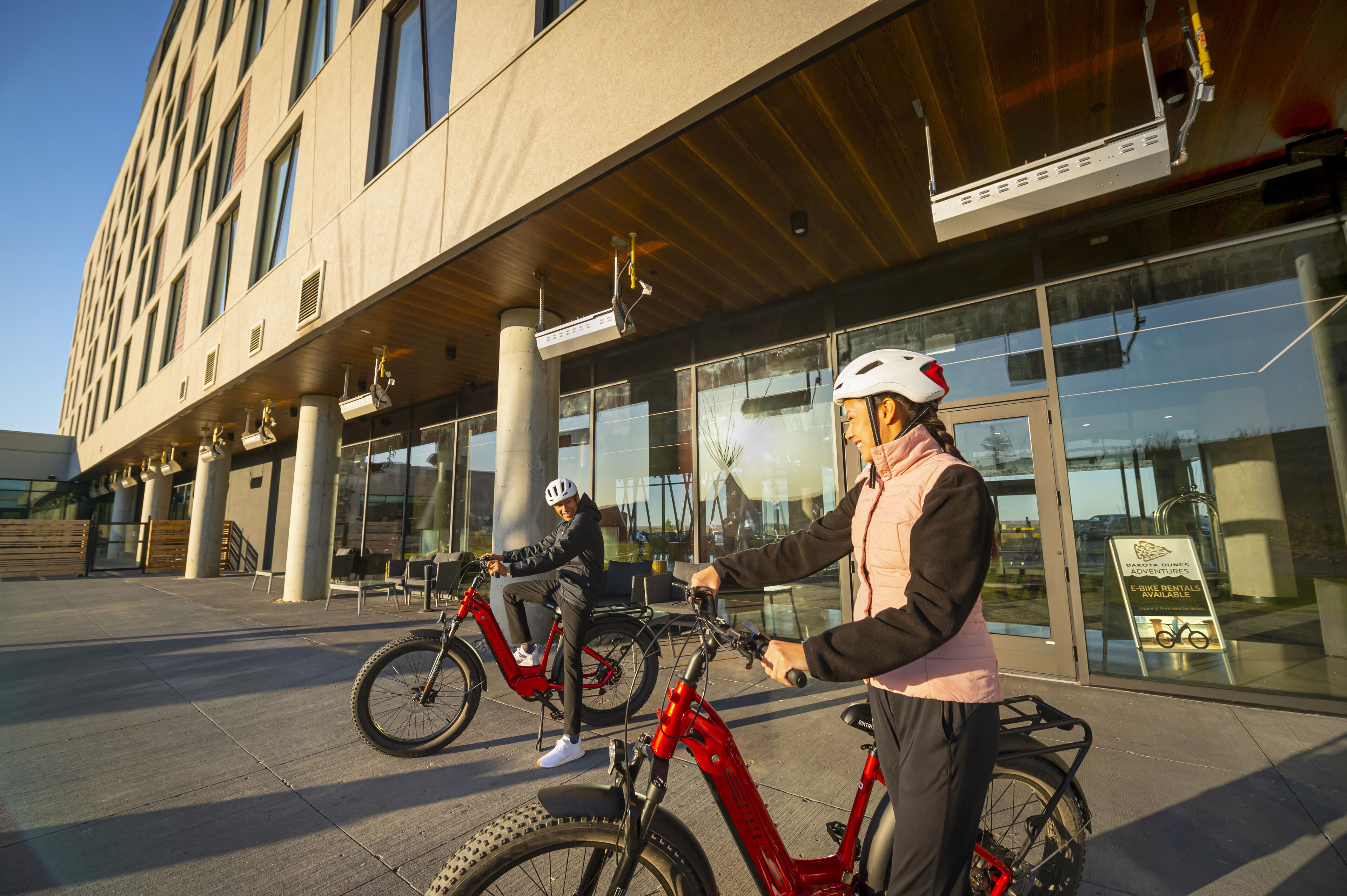 Un bâtiment moderne doté d’une façade en verre et d’une enseigne indiquant la possibilité de louer des vélos électriques.