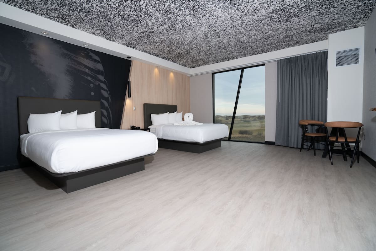 Una habitación de hotel moderna con dos camas, una zona de comedor y un ventanal con vistas.