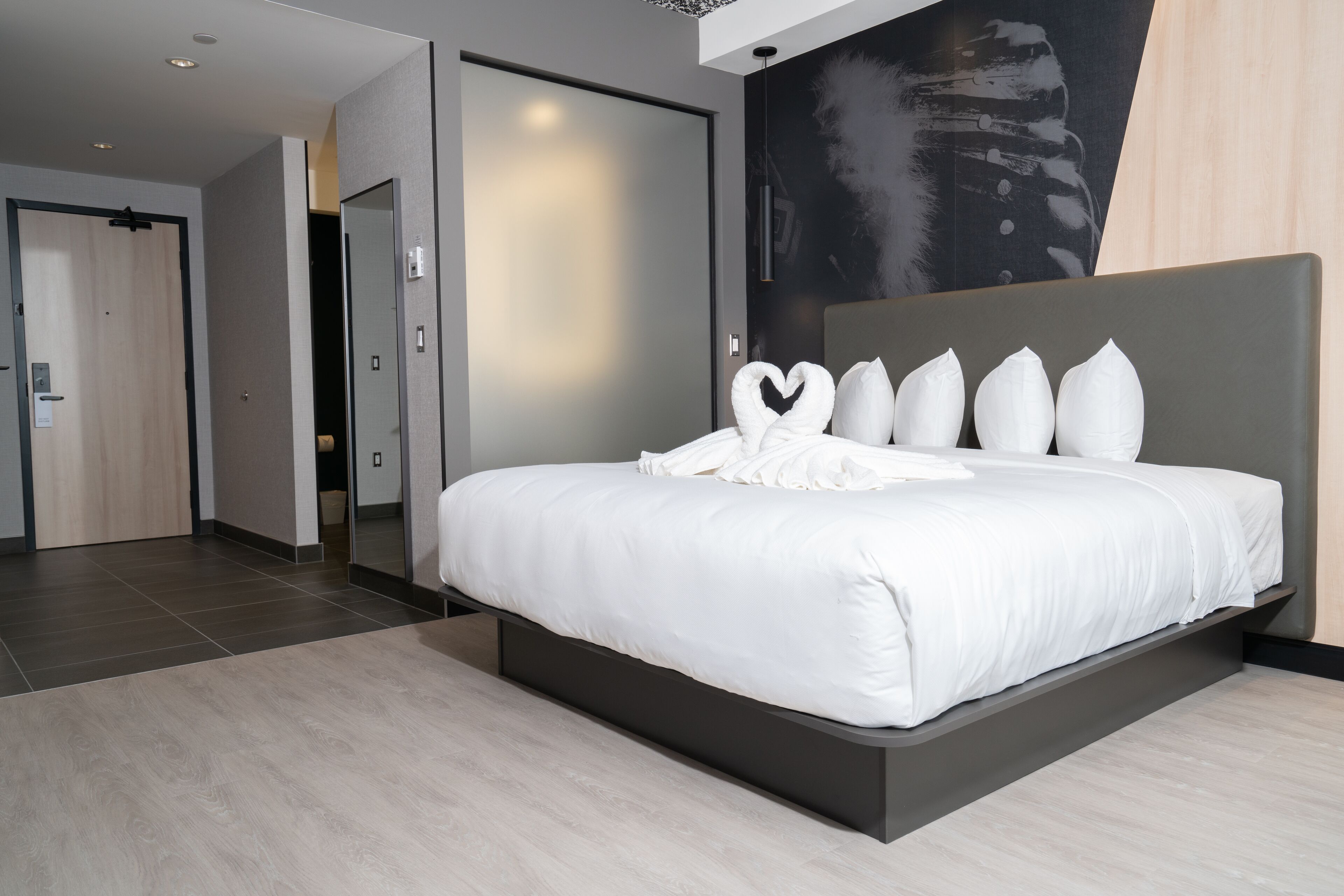 A modern hotel room with a large bed, a dark headboard, and a minimalist design.