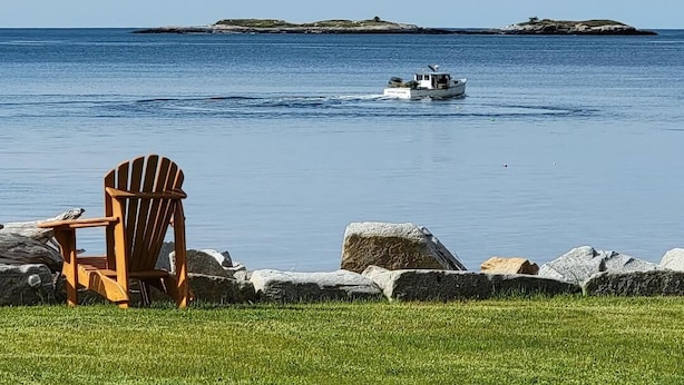 A wooden chair by a grassy shore with a boat on the water and distant islands. - Candy Cove 
Peace and seclusion by the Sea in Maine (Saint George)