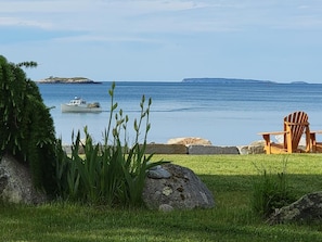 A grassy area with a chair and a boat on the water.