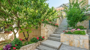 A stone staircase with steps leading up to a building, surrounded by lush green trees and flowering plants. - Apartments Mia (Omis)