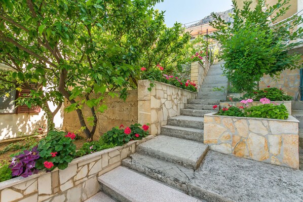 A stone staircase with steps leading up to a building, surrounded by lush green trees and flowering plants.