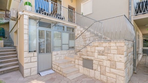A two-story building with a stone facade, a metal staircase, and a balcony with a metal railing. - Apartments Mia (Omis)