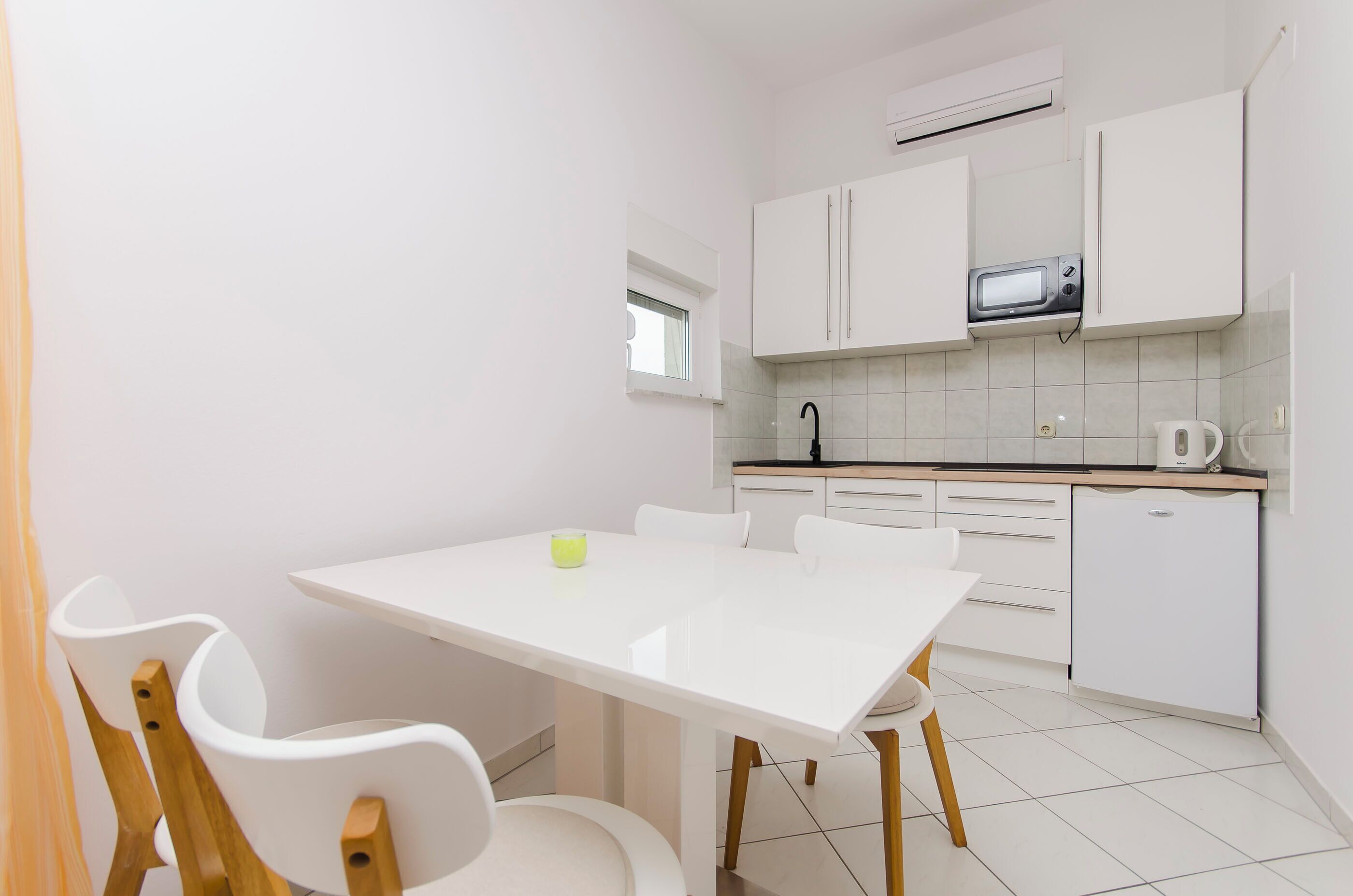 A compact kitchen with white cabinets, a microwave, a kettle, and a small refrigerator.