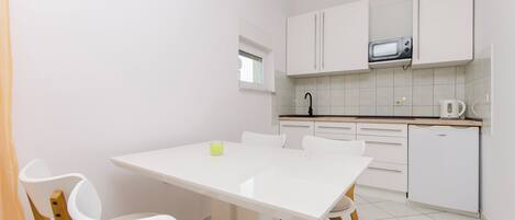 A compact kitchen with white cabinets, a microwave, a kettle, and a small refrigerator.