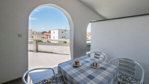 Un balcon avec une table dressée pour deux personnes, une vue sur les bâtiments en arrière-plan et un ciel dégagé.