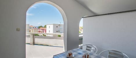A balcony with a table set for two, a view of buildings in the background, and a clear sky.