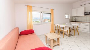 Une pièce moderne et bien éclairée, comprenant un canapé, une petite table, un coin repas avec des chaises, et une cuisine équipée de placards et d’un four à micro-ondes.