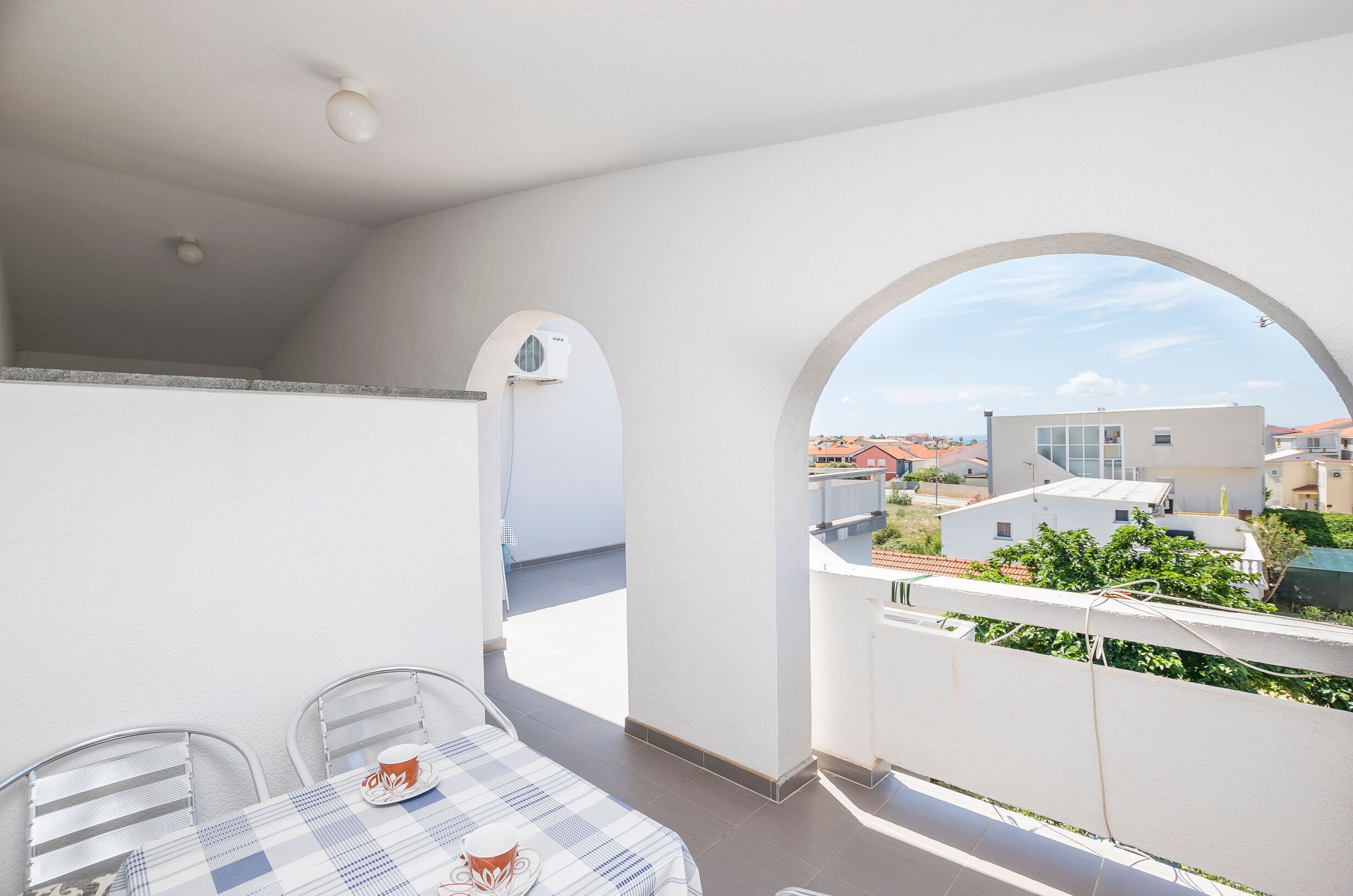 A balcony with a table and chairs, a view of neighboring buildings, and an air conditioning unit.