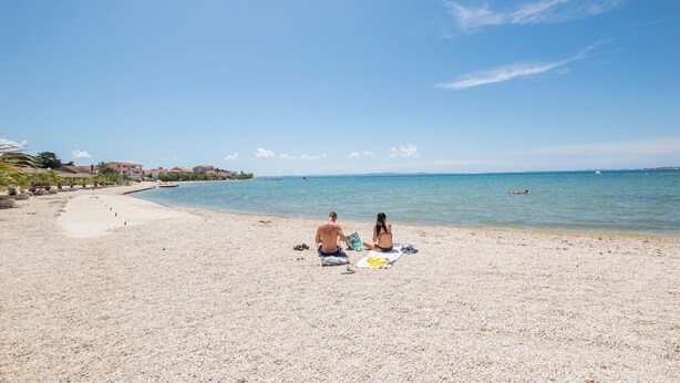 Une plage avec un ciel dégagé, un couple assis sur des serviettes et une mer calme.