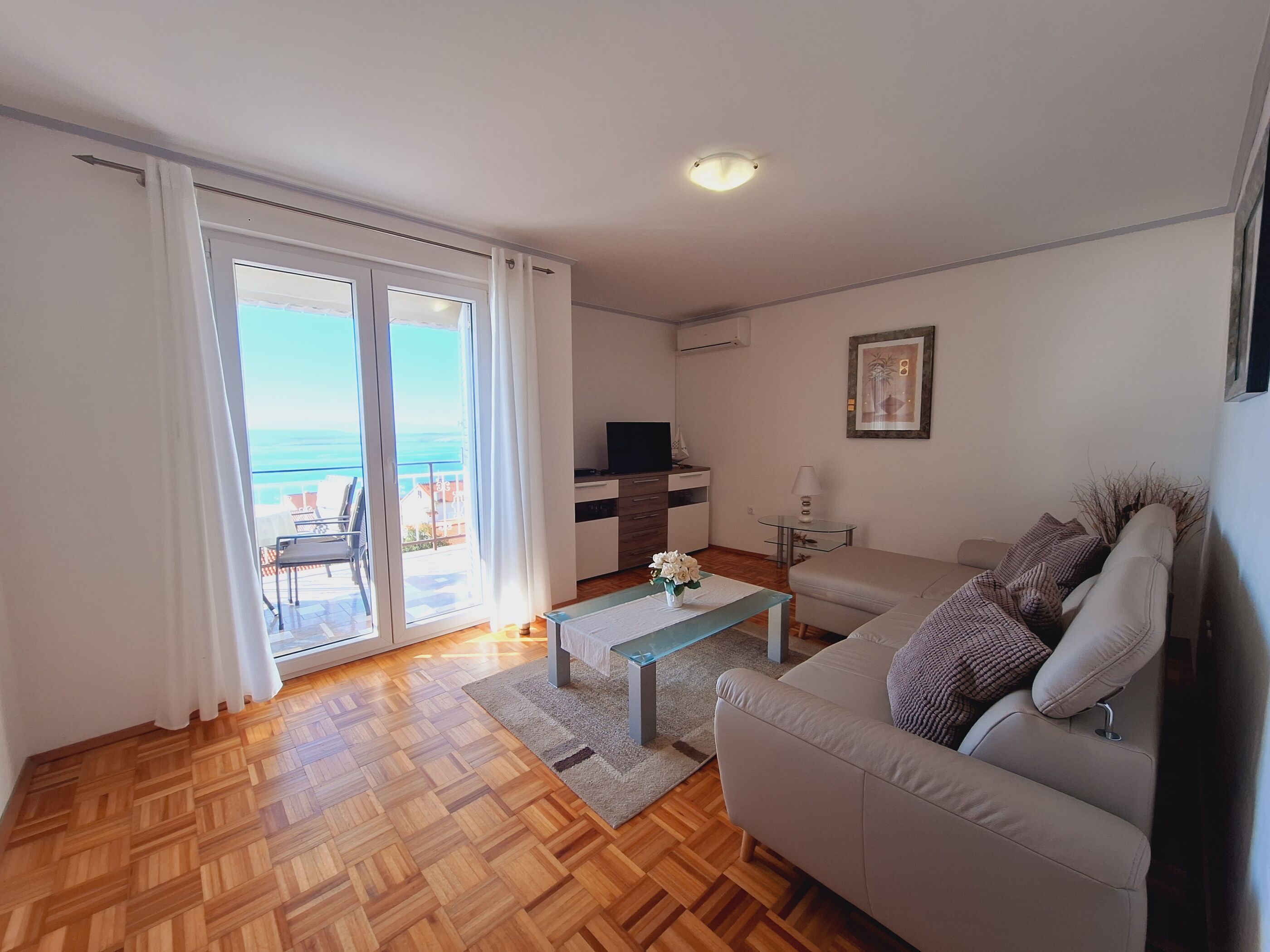 Un salon comprenant un canapé, une table basse, un téléviseur et une vue sur la mer, accessible par une porte coulissante.