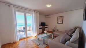 Ein Wohnzimmer mit einer Couch, einem Couchtisch, einem Fernseher und Meerblick durch eine Schiebetür.