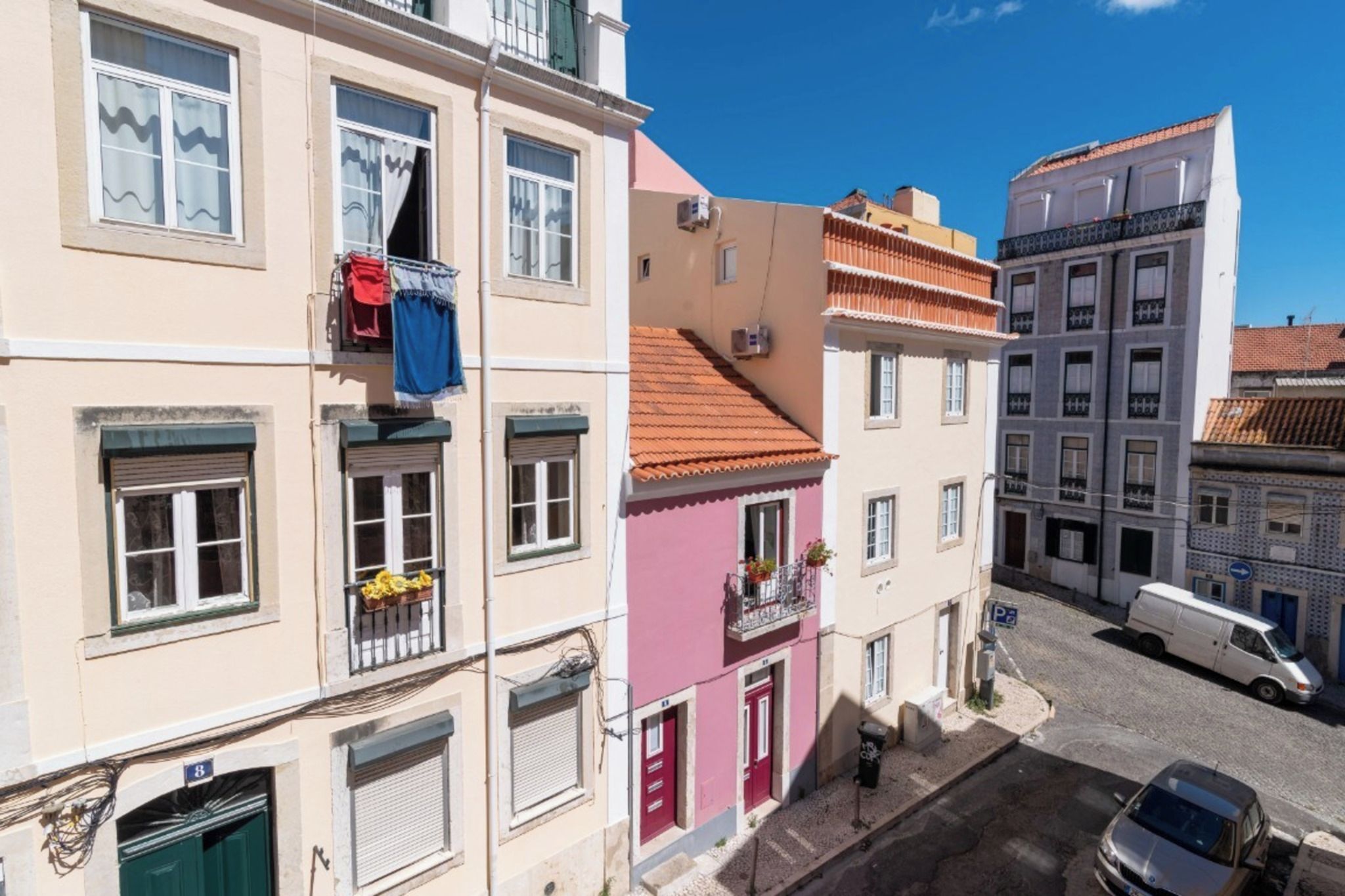Un edificio de varios pisos con balcones, vista a la calle y vehículos estacionados.