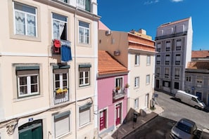 Un immeuble à plusieurs étages doté de balcons, donnant sur la rue et avec des véhicules stationnés devant.
