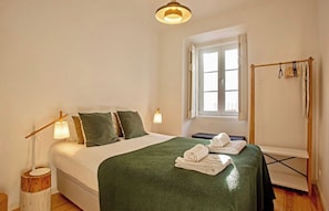 Une chambre d’hôtel avec un lit, une fenêtre, une table de chevet avec une lampe et un porte-serviettes.