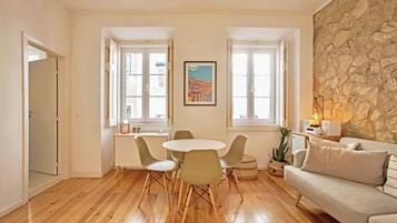 A living room with a stone wall, a round table with chairs, a sofa, and a window with a cityscape view.