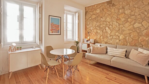 Ein Wohnzimmer mit einer Steinwand, einer Couch, einem Esstisch mit Stühlen und einem Fenster mit Fensterläden.