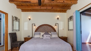 Une chambre avec un plafond en bois, un lit agrémenté d’oreillers à motifs, deux tables de chevet, une chaise et un banc en bois.