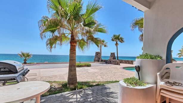 Une terrasse avec un barbecue, des sièges d’extérieur, des palmiers et une vue sur la mer.