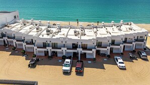 Un hôtel doté d’une terrasse sur le toit offrant une vue sur la mer, de nombreux espaces de stationnement et une plage de sable en arrière-plan.
