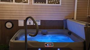 Ein Whirlpool mit digitaler Steuerung, eine Holzterrasse und Lichterketten über Fenstern.