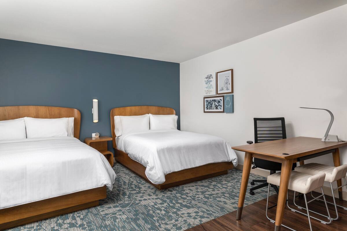 Habitació d'hotel amb dos llits, un escriptori i una cadira.