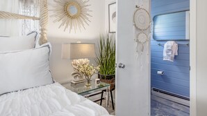 A bedroom with a bed, a vanity with a mirror, a wall-mounted dream catcher, and a blue door. - Charming Ranch on the Cape (Barnstable)