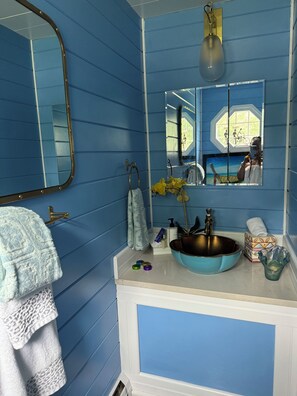 Ein Badezimmer mit blauen Wänden, einem großen Spiegel, einem Waschbecken in Blau und einem Fenster mit Blick auf Fahrräder.