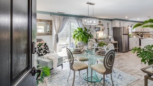 A modern kitchen with a stainless steel refrigerator, a dining area with a glass table and chairs, and a large window with sheer curtains. - Charming Ranch on the Cape (Barnstable)