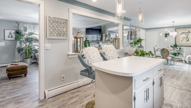 A modern kitchen with a central island, pendant lighting, and a large mirror above the island. - Charming Ranch on the Cape (Barnstable)