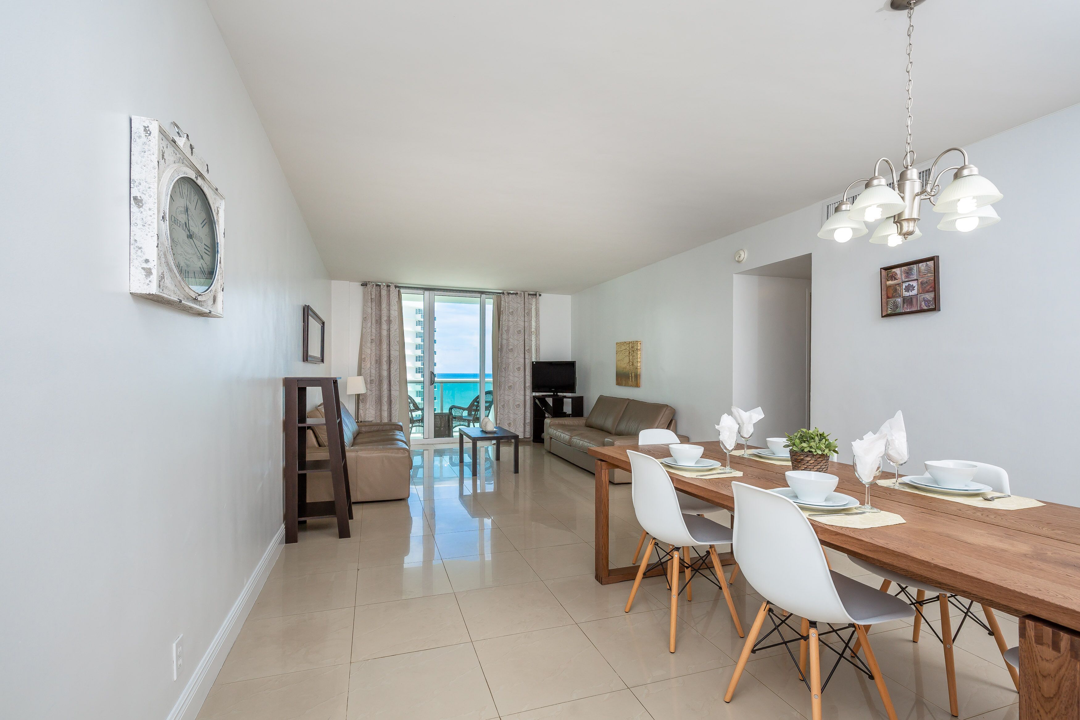 A modern living room with a dining area, a large window, and a view of the ocean.