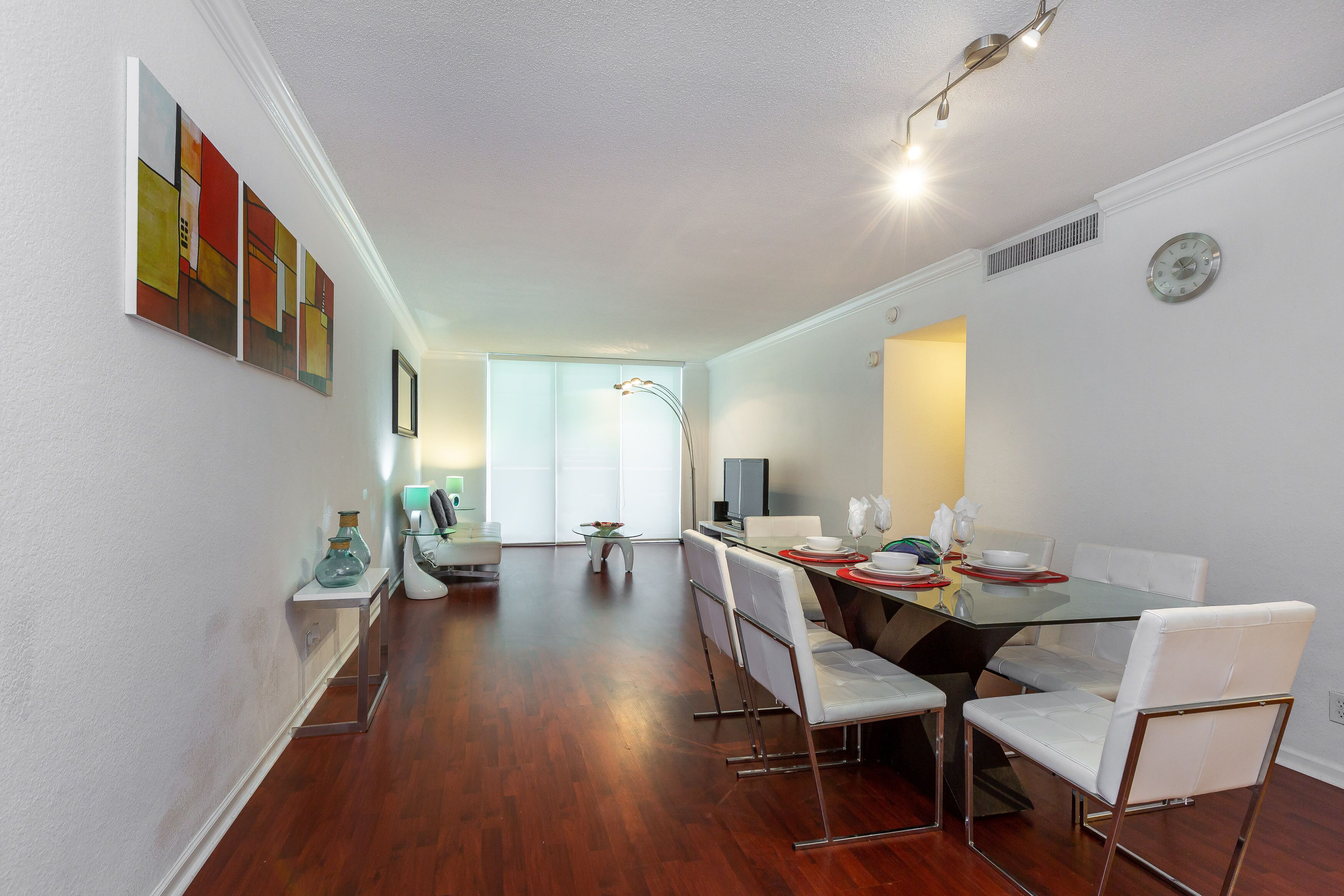 A modern dining area with a glass table, white chairs, and a view to a bright room.