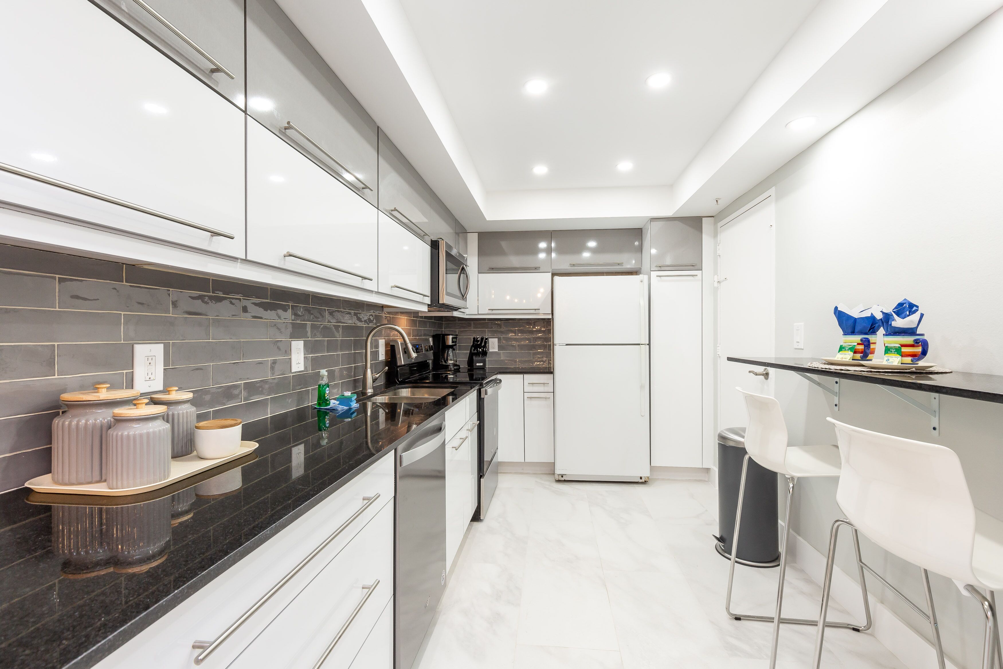 A modern kitchen with white cabinets, a black countertop, and a stainless steel sink.