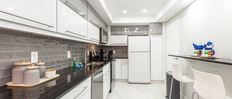 A modern kitchen with white cabinets, a black countertop, and a stainless steel sink.
