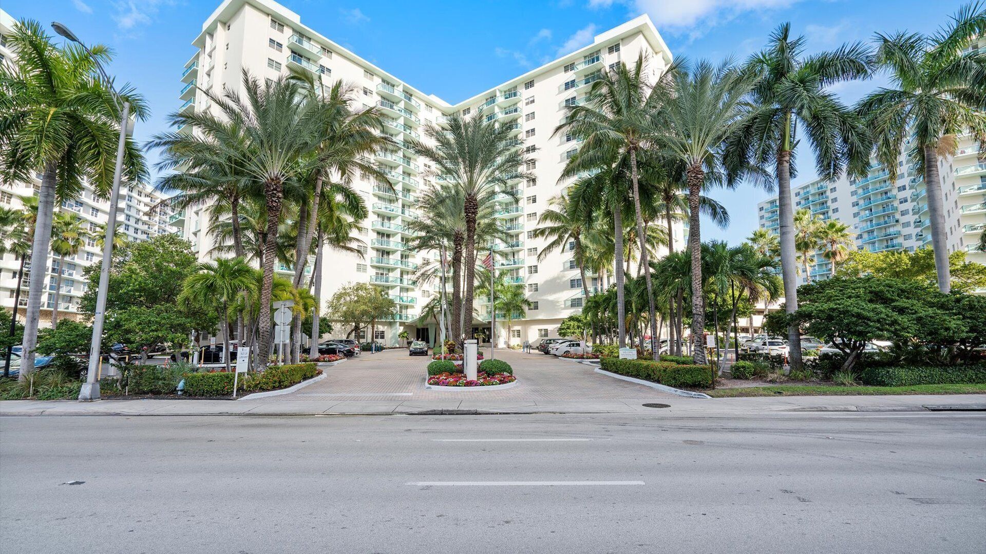 A modern hotel with a central courtyard, surrounded by palm trees and a clear sky.