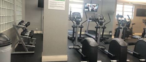 Une salle de sport équipée de divers appareils d’exercice, notamment des tapis de course, des vélos elliptiques et des bancs de musculation.