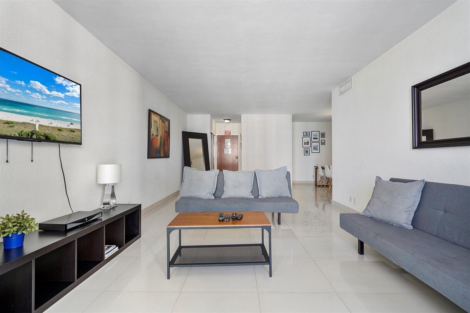 A modern living room with a grey sofa, a wooden coffee table, and a TV displaying a beach scene.