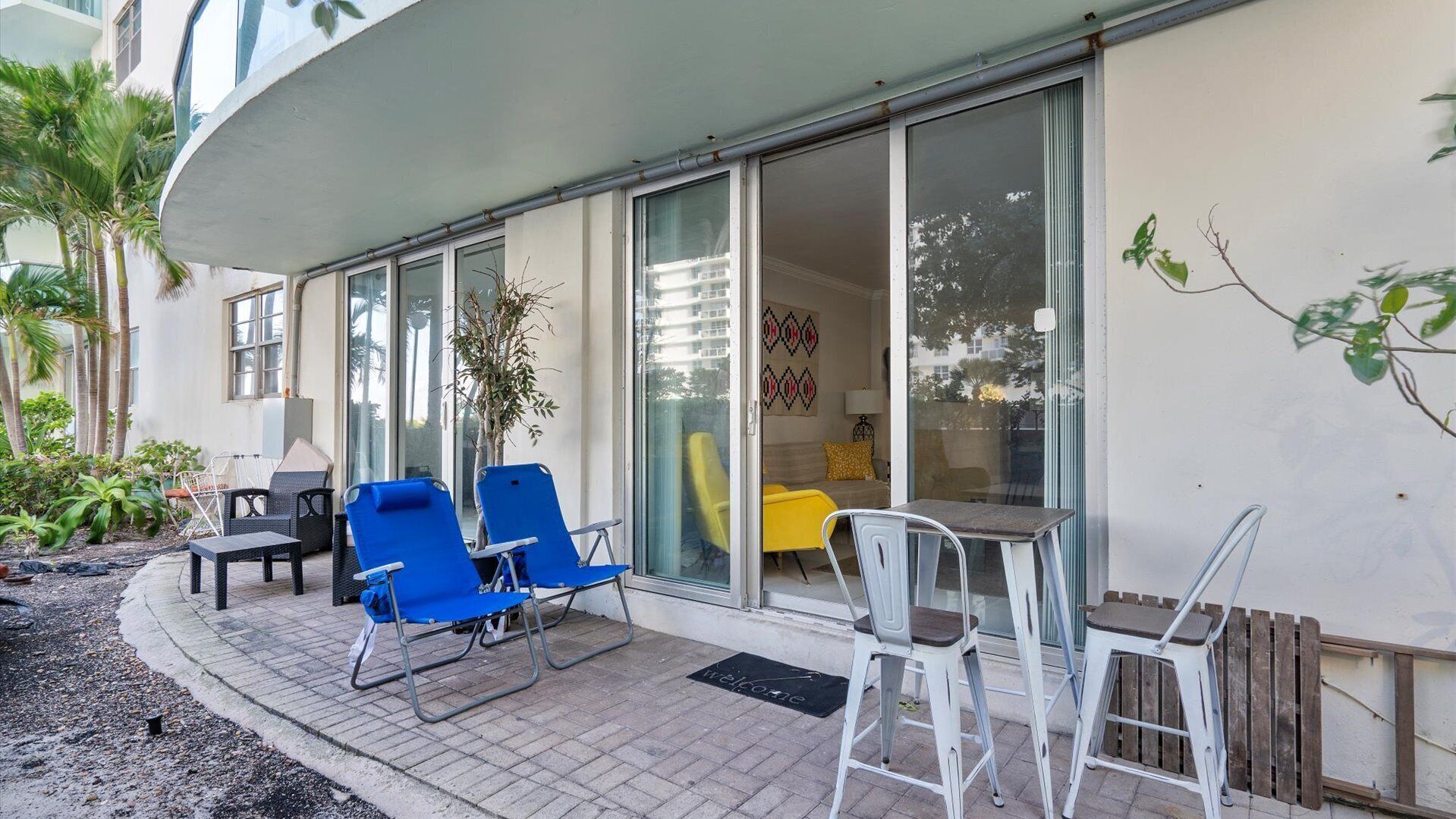 A modern building with a patio area featuring blue and white chairs, a small table, and a potted plant.