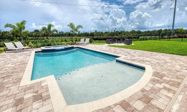 Una piscina rectangular con una sección curva, rodeada por un patio de ladrillo.