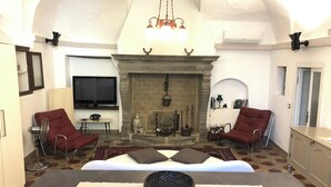 A living room with a fireplace, two red armchairs, a sofa, a television, and a dining table with a woven bowl.