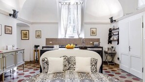 A bedroom with a large bed, a desk, a window with curtains, a kitchen area, and a bathroom.