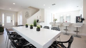 A modern kitchen with white countertops, black chairs, and a large island with plants. - Contemporary Disney Vacation Home - 5 min to Disney (Kissimmee)