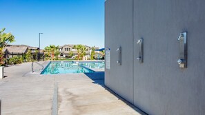 Una piscina con plataforma de concreto, un letrero de precaución y un edificio con puerta metálica.