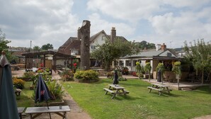 A courtyard with picnic tables, a covered seating area, and a building with a garden. - Balfour Arms (Sidmouth)