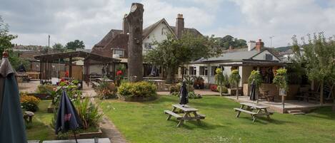 A courtyard with picnic tables, a covered seating area, and a building with a garden.