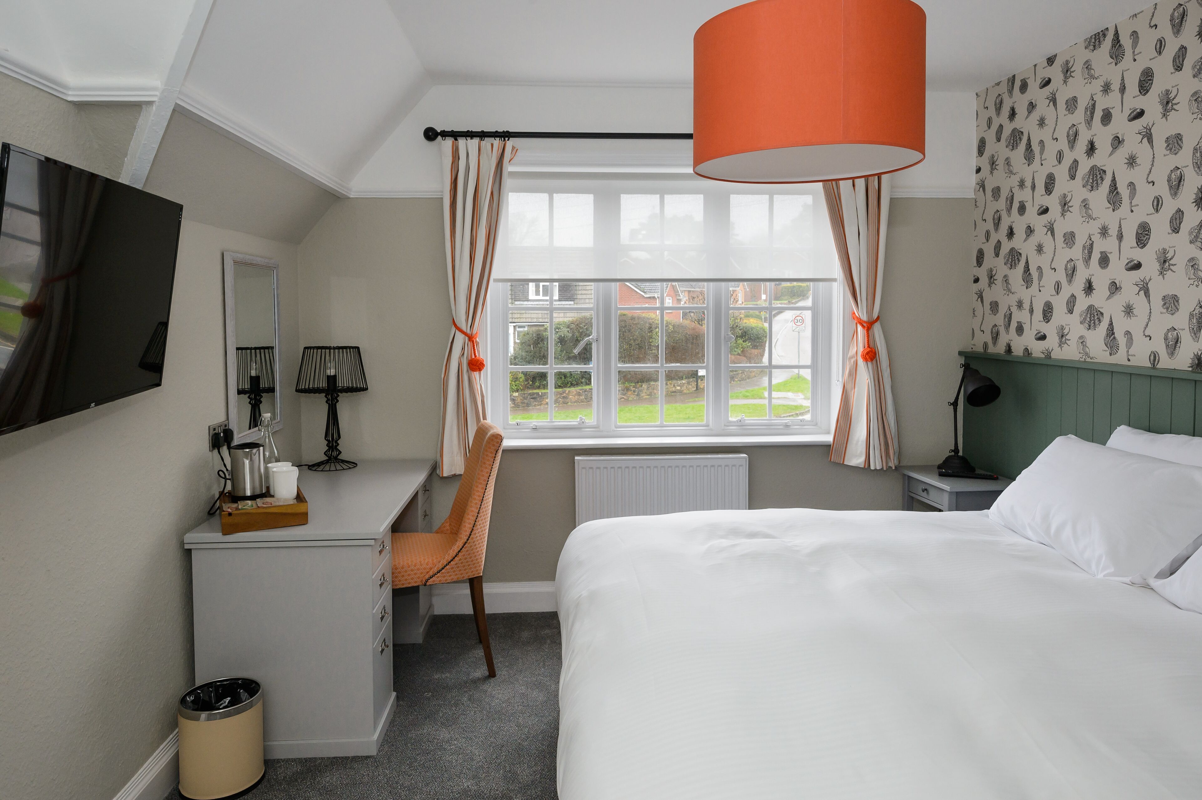 A hotel room with a bed, desk, chair, and a window with curtains.