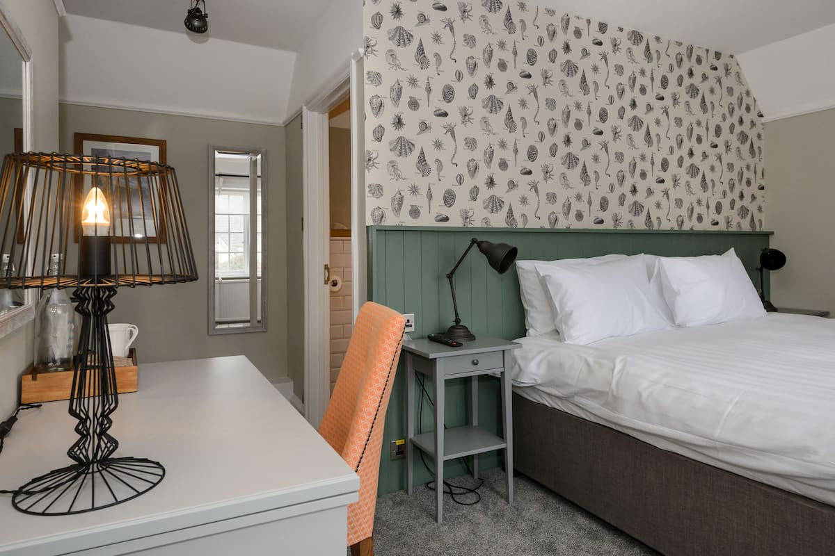 A hotel room with a bed, a desk, a chair, a lamp, and a wall with a leaf pattern.