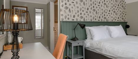 A hotel room with a bed, a desk, a chair, a lamp, and a wall with a leaf pattern.