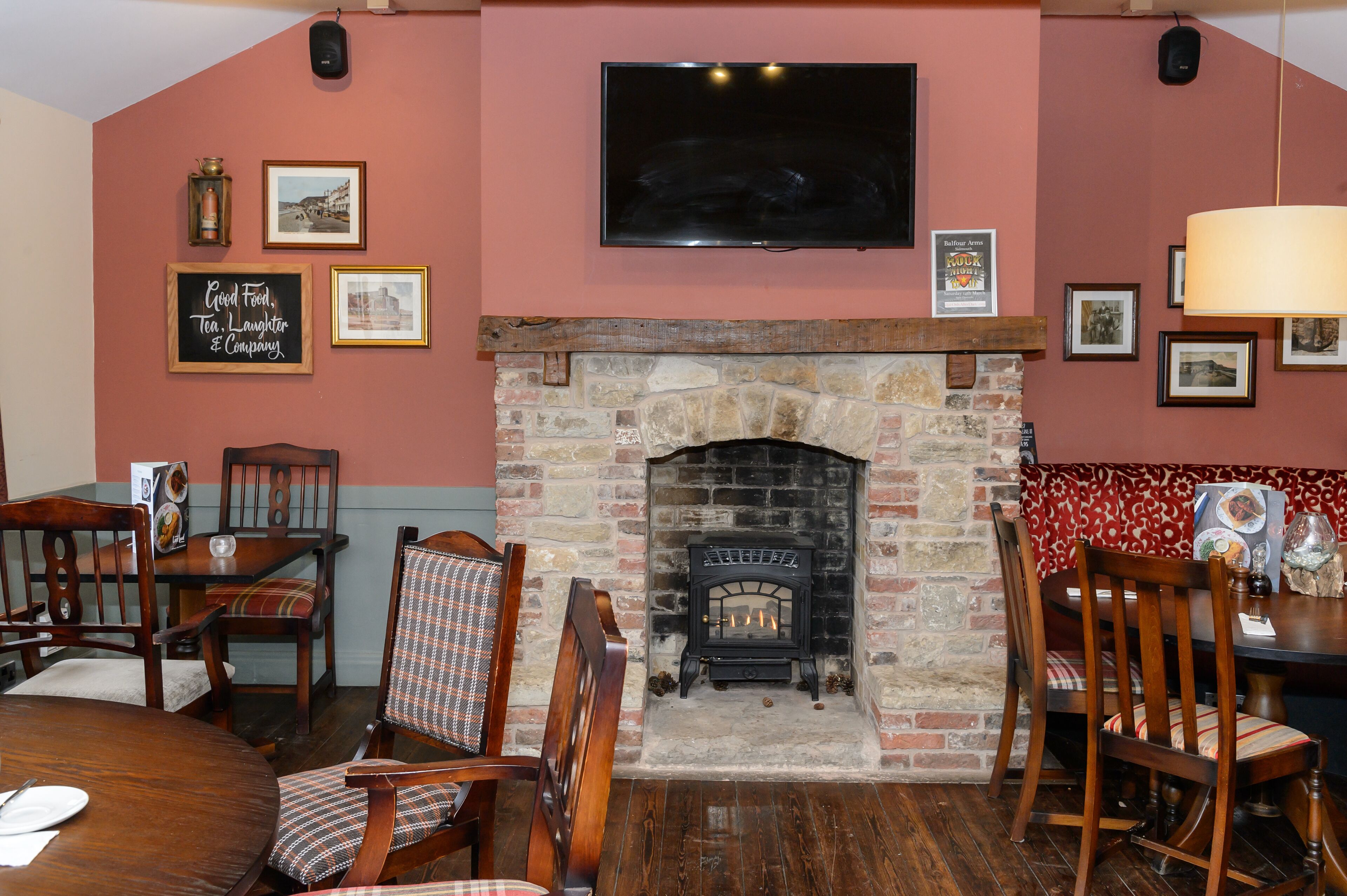 A cozy dining area with a stone fireplace, wooden chairs, and a television mounted on the wall.